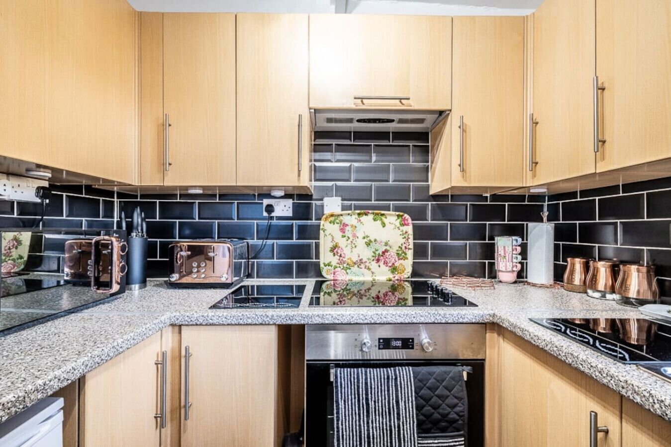 A kitchen with wooden cabinets, a black tiled backsplash, a stainless steel stove, and a floral-patterned chair.