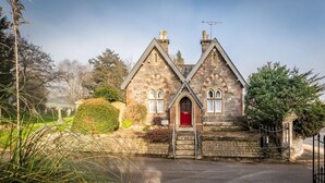 A stone building with a red door, surrounded by a stone wall and a metal gate. - Charming character lodge in cemetery grounds (Devon)