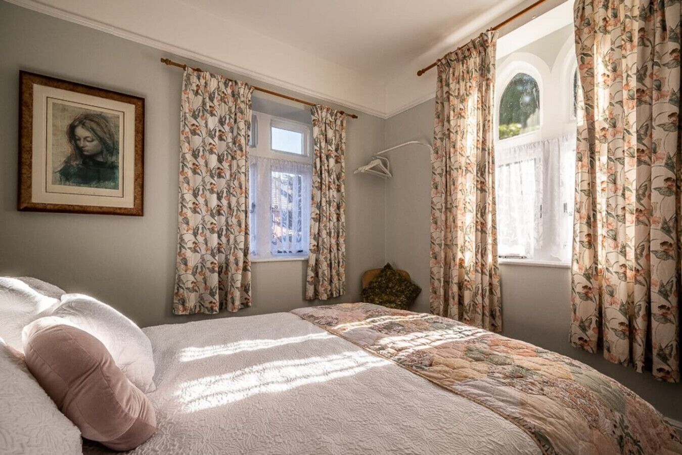 A bedroom with a bed, floral curtains, a window, and a framed picture on the wall.