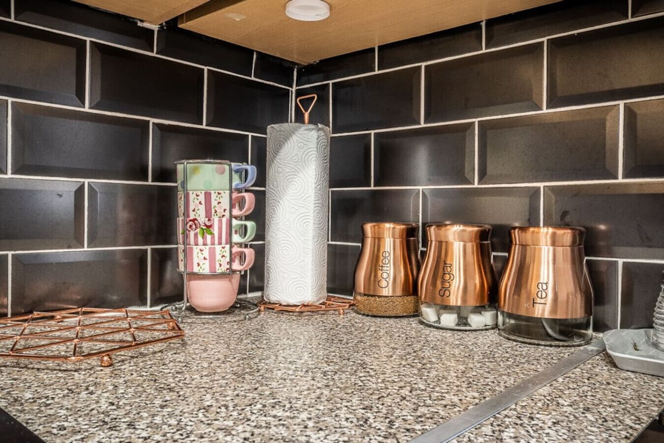 A kitchen with a granite countertop, black tiled backsplash, and a coffee machine.