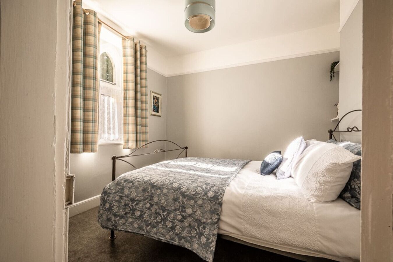 Een slaapkamer met een bed, een raam met gordijnen, een wandlamp en een deur.