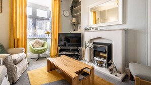 A living room with a fireplace, a green armchair, a wooden coffee table, and a television. - Charming character lodge in cemetery grounds (Devon)