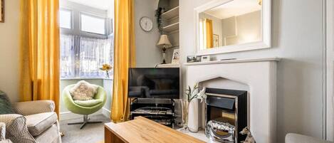 A living room with a fireplace, a green armchair, a wooden coffee table, and a television.
