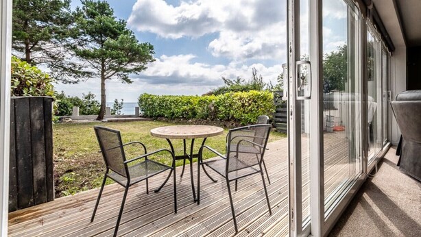 A deck with a table and chairs, overlooking a grassy area with trees and a view of the sea. - 2 BR Seaside Flat/ Parks 2 - Garden & Ocean Views (Dawlish)