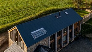 Un bâtiment moderne doté d’un toit en pente, de grandes fenêtres et offrant une vue sur un champ verdoyant.