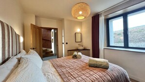 Une chambre d’hôtel avec un grand lit, une table de chevet avec une lampe, une vue sur l’extérieur et une porte donnant accès à la salle de bain.