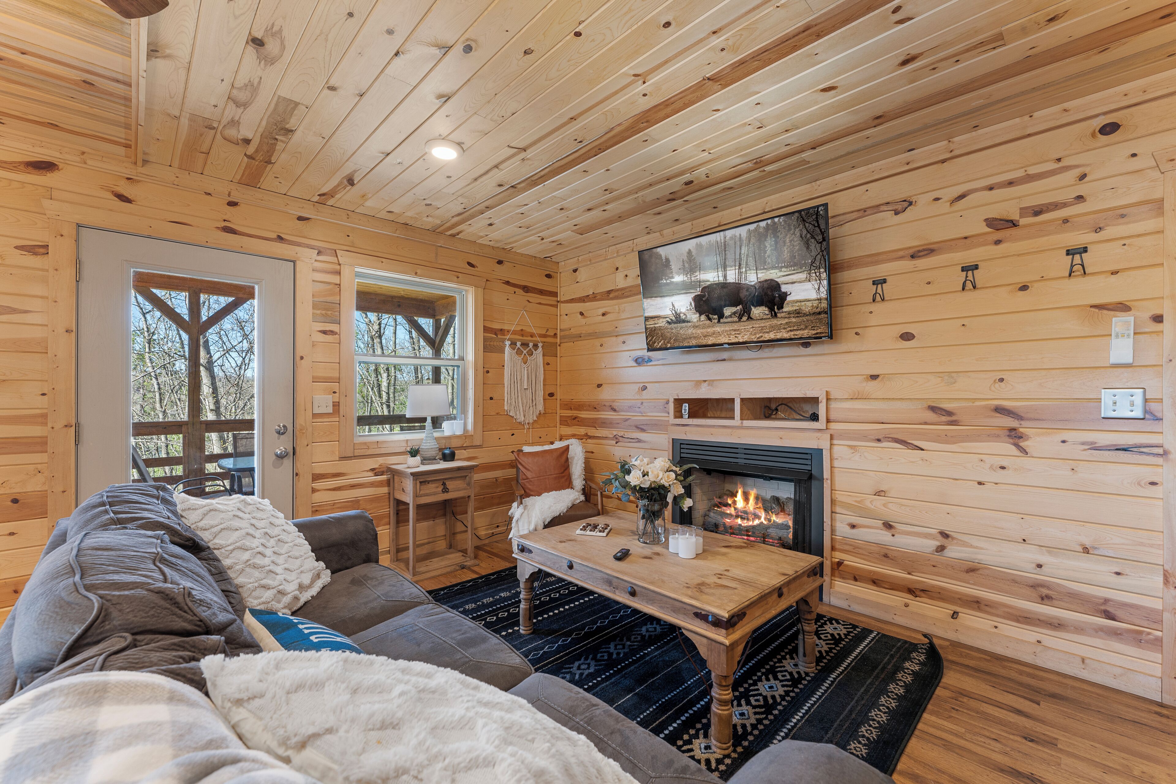 A cozy cabin interior with a fireplace, wooden walls, a sofa, and a dining table.