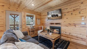 Interior acogedor de una cabaña con chimenea, paredes de madera, un sofá y una mesa de comedor.