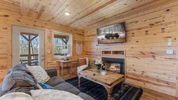 A cozy cabin interior with a fireplace, wooden walls, a sofa, and a dining table.