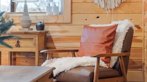 Interior de una cabaña de madera con una silla, una mesita y una lámpara.