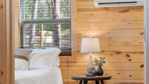 Un dormitorio con cama, mesita de noche con lámpara y ventana con persianas.