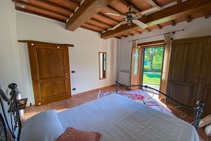 Una camera da letto con un letto, travi a vista in legno, una ventola a soffitto, una finestra e una porta.