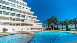 A swimming pool with a diving board, surrounded by palm trees and a building with multiple balconies. - WELCS APARTAMENTO 224 EMP con TERRAZA (Rosas / Roses)