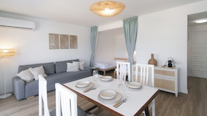A modern living room with a dining table set for four, a sofa, a lamp, and a decorative wall piece. - WELCS APARTAMENTO 224 EMP con TERRAZA (Rosas / Roses)
