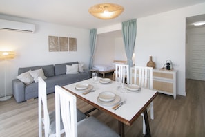 A modern living room with a dining table set for four, a sofa, a lamp, and a decorative wall piece.