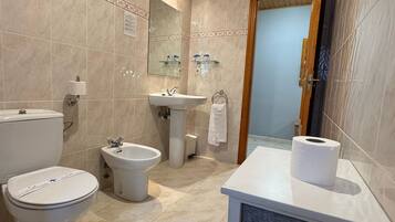 A bathroom with a toilet, bidet, sink, and mirror.