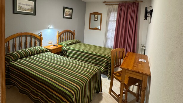 A room with two beds, a wooden table, and a chair. - HOSTAL MARBORE (Bielsa)