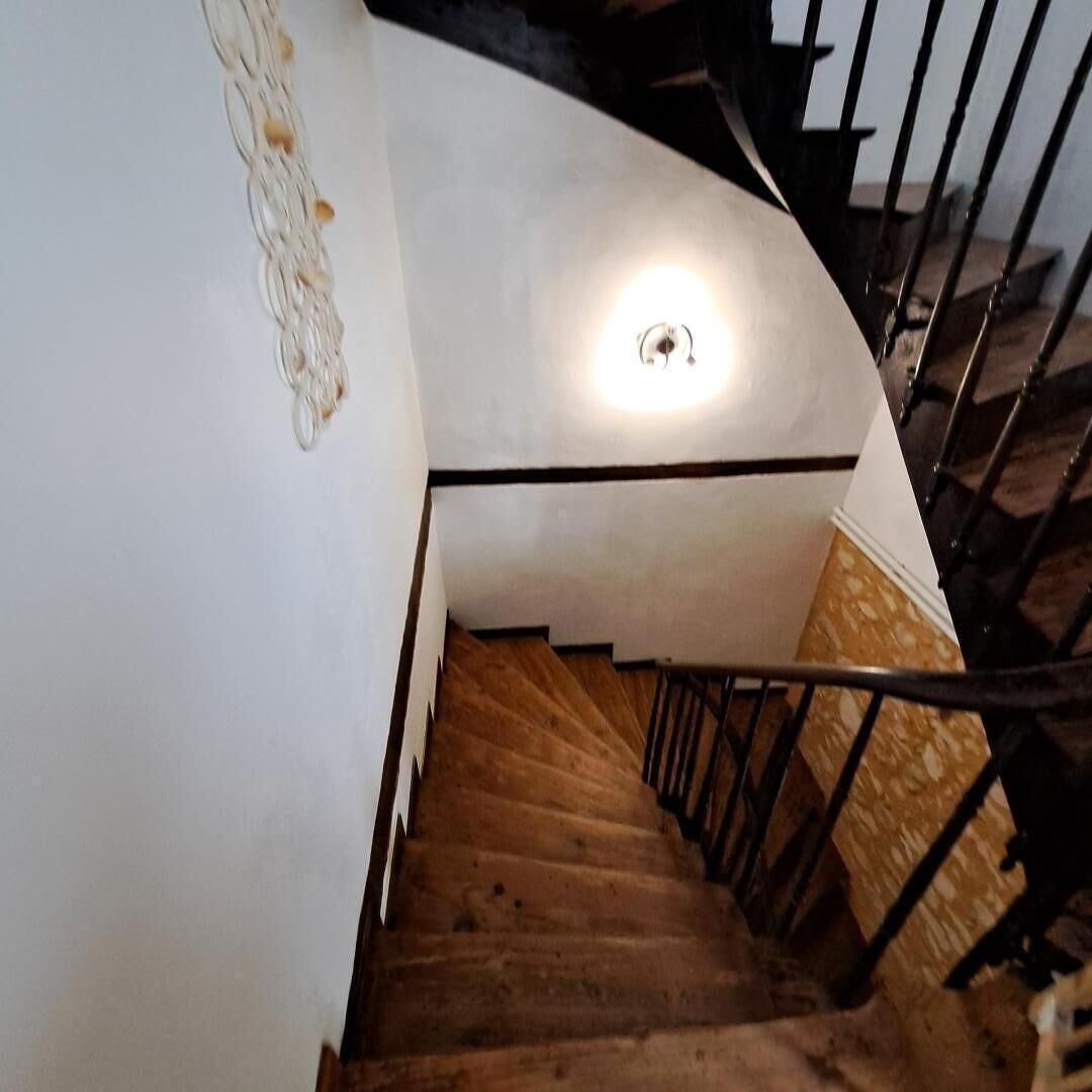 A wooden staircase with a handrail, white walls, and a light fixture at the top.