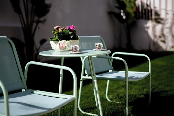 Un petit espace extérieur aménagé avec deux chaises et une table, un pot de fleurs et deux tasses.