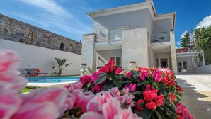Uma casa moderna de dois andares com piscina, varanda e muro de pedra.