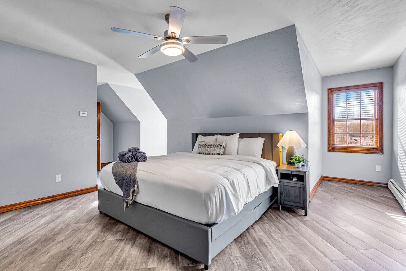 A bedroom with a bed, a nightstand, a ceiling fan, a window, and a skylight.