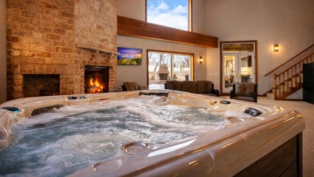 A hot tub in a room with a stone fireplace, wooden beams, and a view of the outdoors.