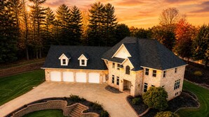 A large, two-story house with a stone facade, multiple garage doors, and a well-manicured lawn.
