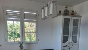 Una cocina con encimera negra, armarios blancos, una ventana con persianas y una pequeña olla roja sobre la encimera.