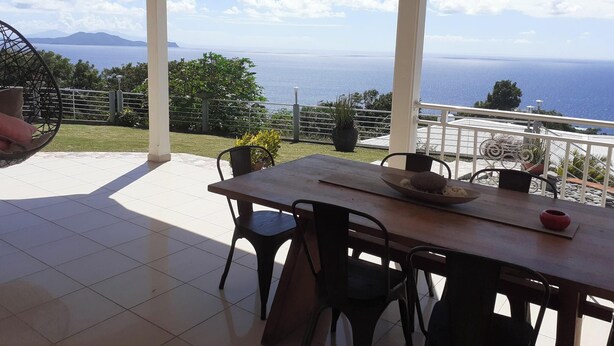 Un patio techado con mesa y sillas, con vistas panorámicas al mar y las montañas.