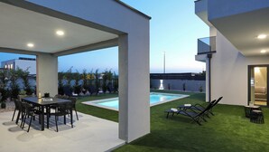 A modern outdoor patio with a dining table and chairs, a pool, and lounge chairs. - Villa Cvit Mediterana with heated pool (Poljica-Brig)