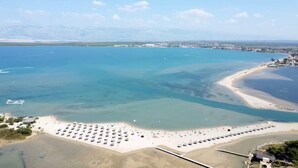 An aerial view of a beach with rows of sunbeds and umbrellas, a clear blue sea, and a distant cityscape. - Villa Cvit Mediterana with heated pool (Poljica-Brig)