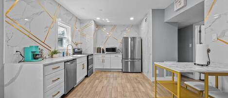 A modern kitchen with marble walls, wooden flooring, and stainless steel appliances.