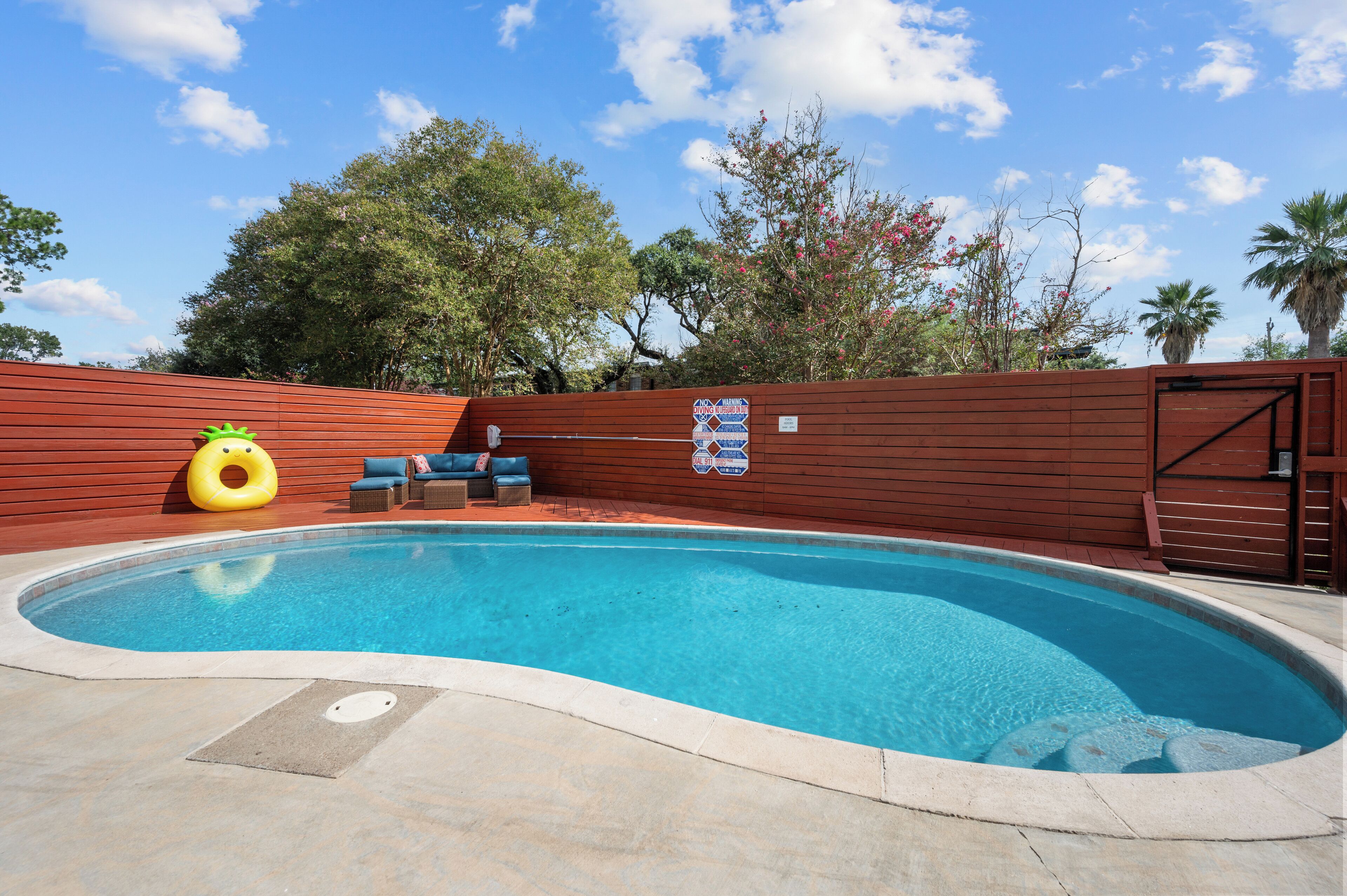 Ein Swimmingpool mit Holzterrasse, Liegestühlen und einem gelben Schwimmreifen.