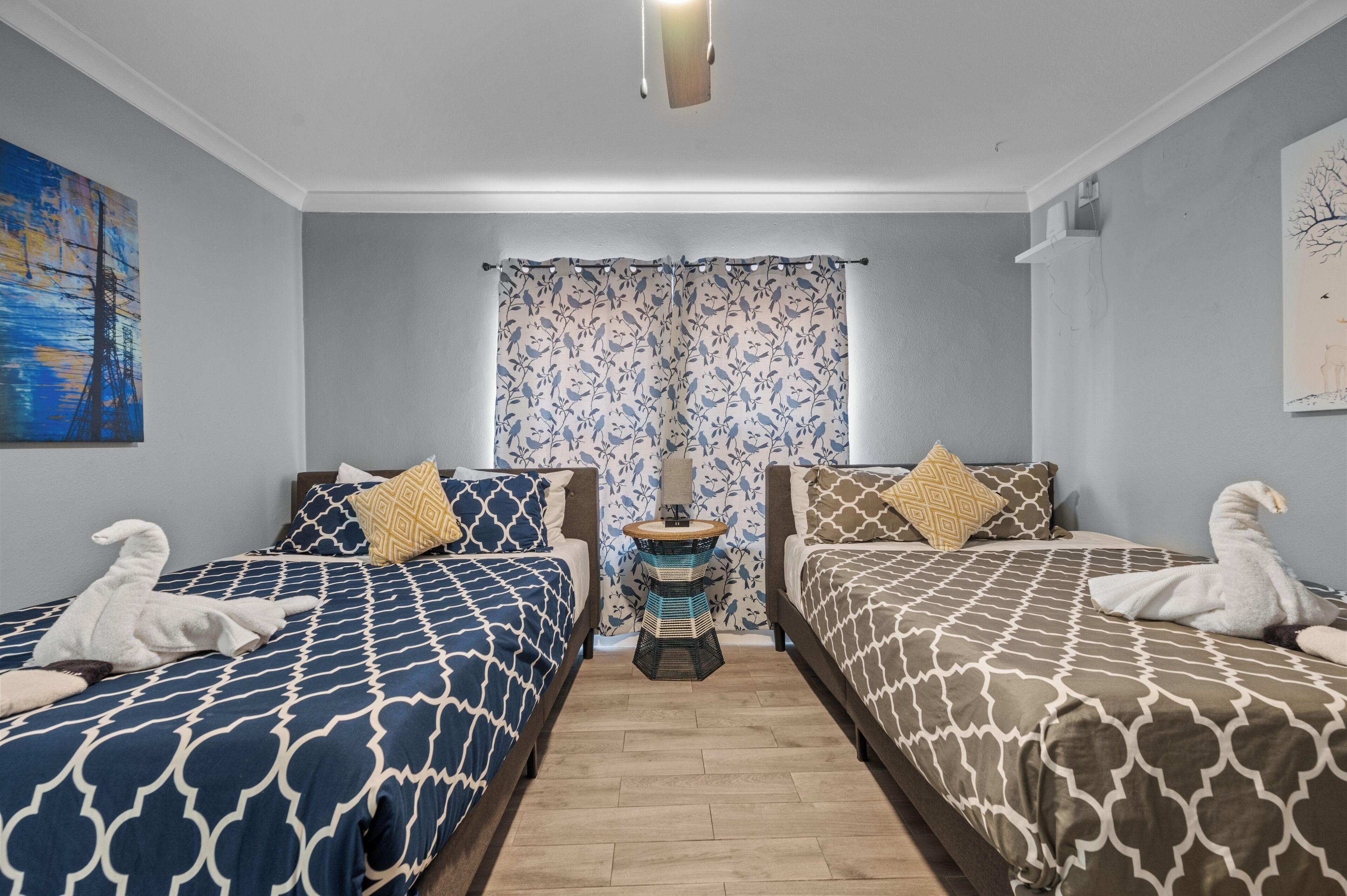 Habitación de hotel con dos camas, cada una con ropa de cama estampada, una mesita auxiliar pequeña y una cortina con diseño floral.