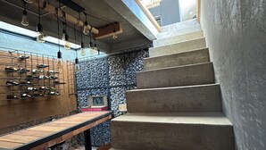 Eine Treppe führt zu einem Erkerbereich mit einem Holztisch und Stühlen, einer Steinwand und hängenden Leuchten.