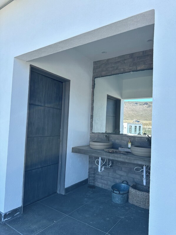 Un baño moderno con un espejo grande, dos lavamanos y una puerta oscura.