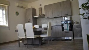 Cocina moderna con gabinetes grises, horno de acero inoxidable y comedor con sillas blancas y una mesa.