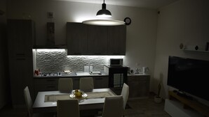 Una cocina moderna con comedor, que incluye una isla grande, sillas blancas y un televisor de pantalla plana.