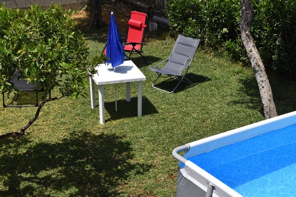 A backyard with a pool, a table with an umbrella, and two lawn chairs.