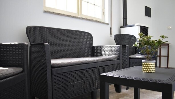 Un salón moderno con un sofá de mimbre oscuro, un sillón a juego y una mesita con un jarrón decorativo.