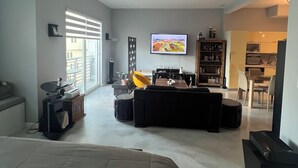 A spacious living area with a large bed, a sofa, a television, and a kitchen in the background.