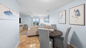 A dining area with a round table, grey upholstered chairs, and artwork on the walls. - Grand Caribbean 312 2 Bed 2 Bath - Great View! (Orange Beach)