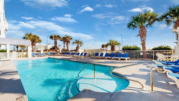 A swimming pool with blue water, surrounded by white lounge chairs and palm trees. - Grand Caribbean 312 2 Bed 2 Bath - Great View! (Orange Beach)