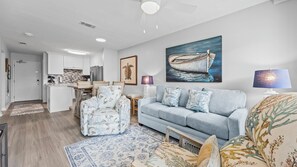 A modern living room with a light blue sofa, patterned armchairs, and a dining area with white cabinets and a kitchen island. - Gulf Shores Plantation 4112 Ft Morgan Oasis (Gulf Shores)