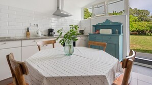 A kitchen with a table set for two, a blue cabinet, and a view of the garden. - Holiday Home 'Casa Do Caseiro' with Mountain View, Private Garden and Wi-Fi (Ponta Delgada)