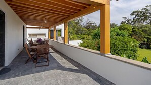 Una terrazza esterna con una pergola in legno, un tavolo da pranzo con sedie e vista su un giardino rigoglioso.