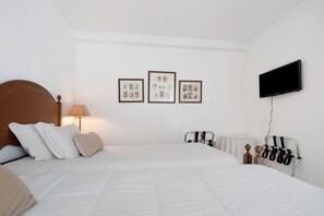 Un dormitorio con una cama, un televisor montado en la pared y tres cuadros enmarcados sobre la cama.