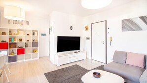 Ett modernt vardagsrum med en platt-TV, en vit soffa, ett soffbord och en bokhylla.