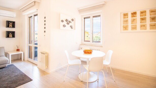 Ett ljust och modernt vardagsrum med ett runt, vitt bord och stolar, en grå soffa och ett litet vitt sidobord.