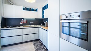 Ett modernt kök med en inbyggd ugn, en mikrovågsugn och en gasspis. Köket har ett svart stänkskydd och en mönstrad matta på golvet.